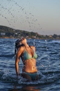 bronzed woman with green bikini on with summer glow tan in sea flicking hair back