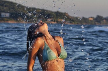 bronzed woman with green bikini on with summer glow tan in sea flicking hair back