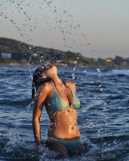 bronzed woman with green bikini on with summer glow tan in sea flicking hair back